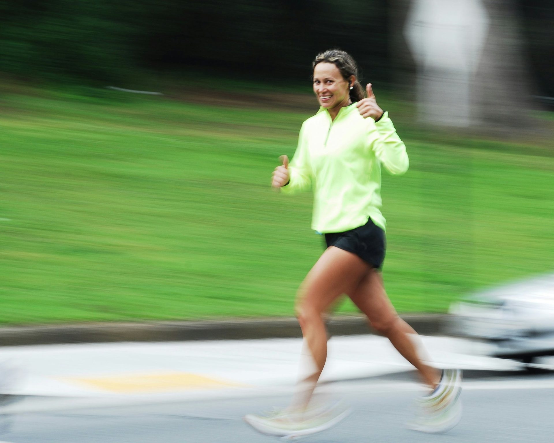 A woman jogging on a street and giving a thumbs up