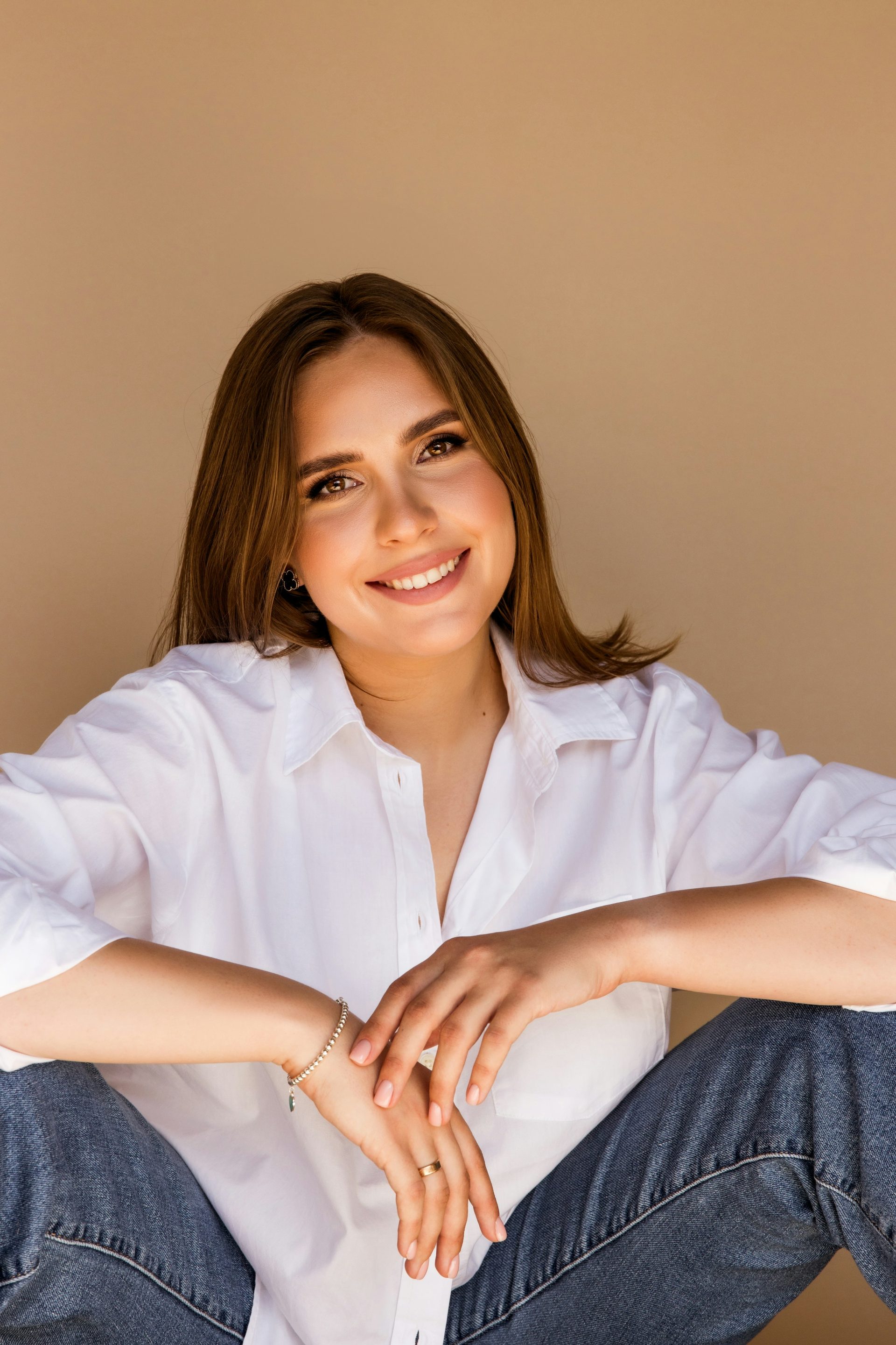 A young woman in a white shirt smiling against a plain tan wall