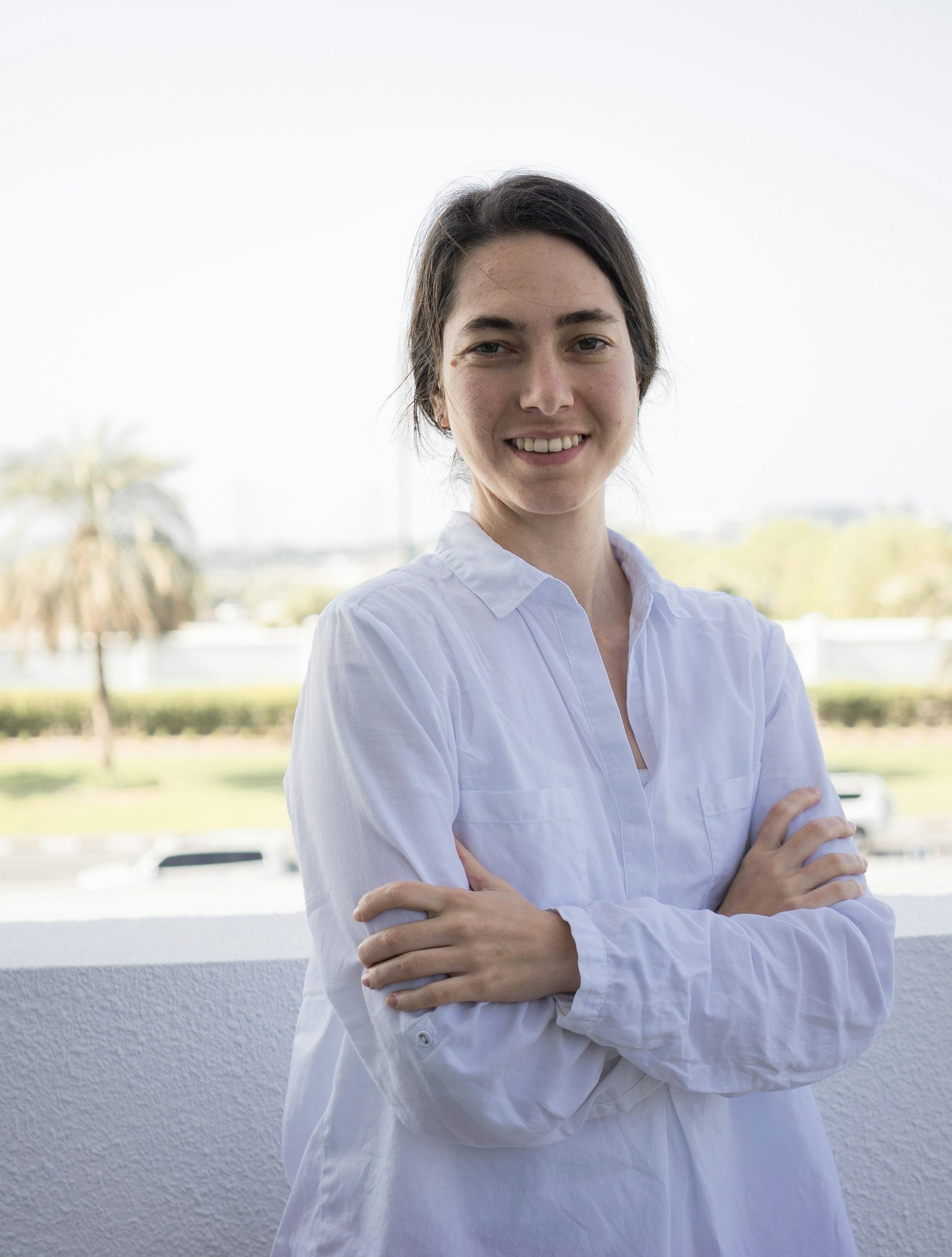 A woman in a white shirt, arms folded, smiling on a rooftop