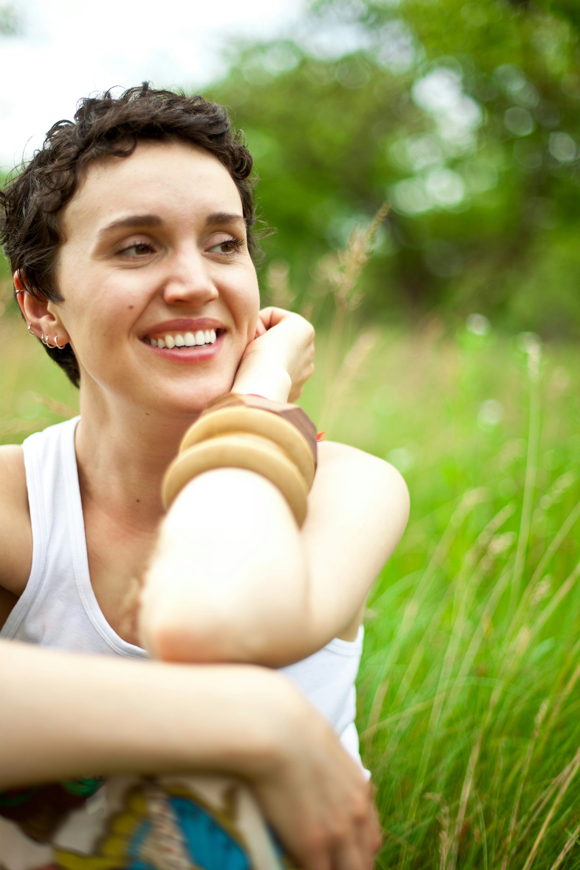 A woman smiling in a summer meadow, hand resting on her chin