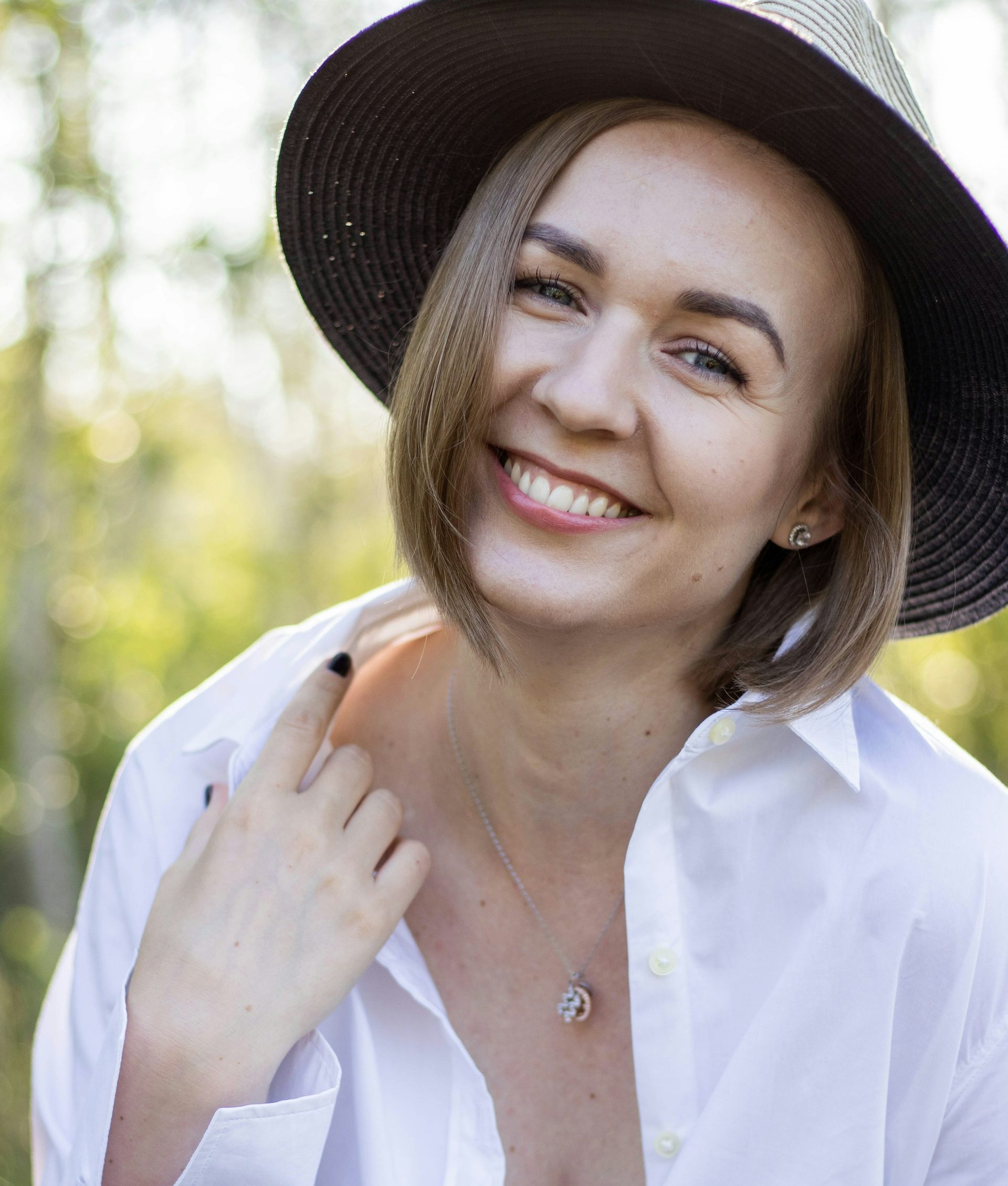 A woman in a wide-brimmed hat smiling under the trees