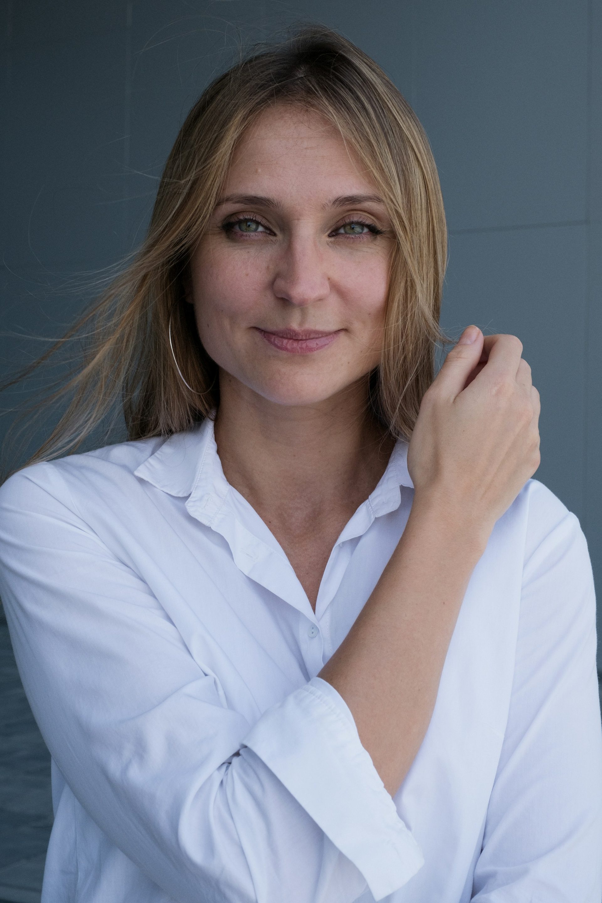 A woman in a white shirt by a blue wall, hair loose in the wind