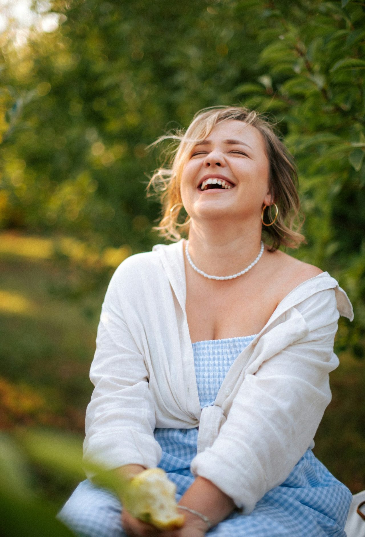 A woman laughing with an apple in an orchard