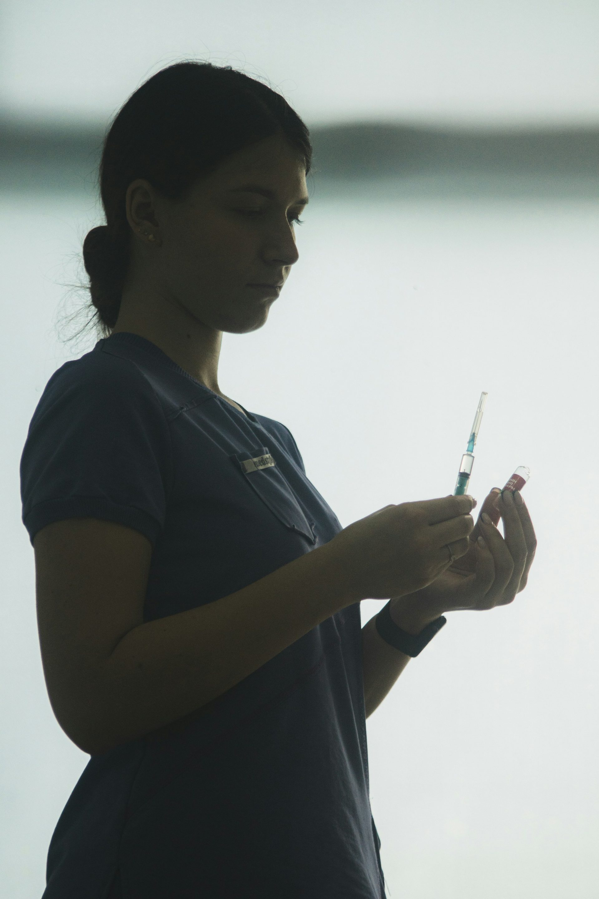 A care provider in scrubs, in silhouette, drawing up a shot