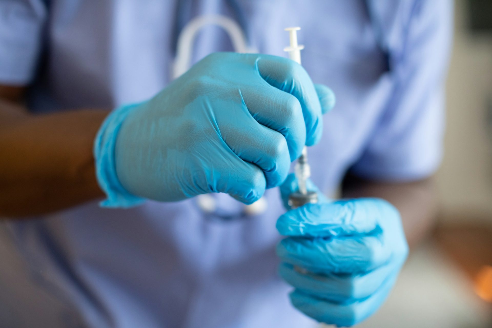 Gloved hands drawing from a small vial into a syringe