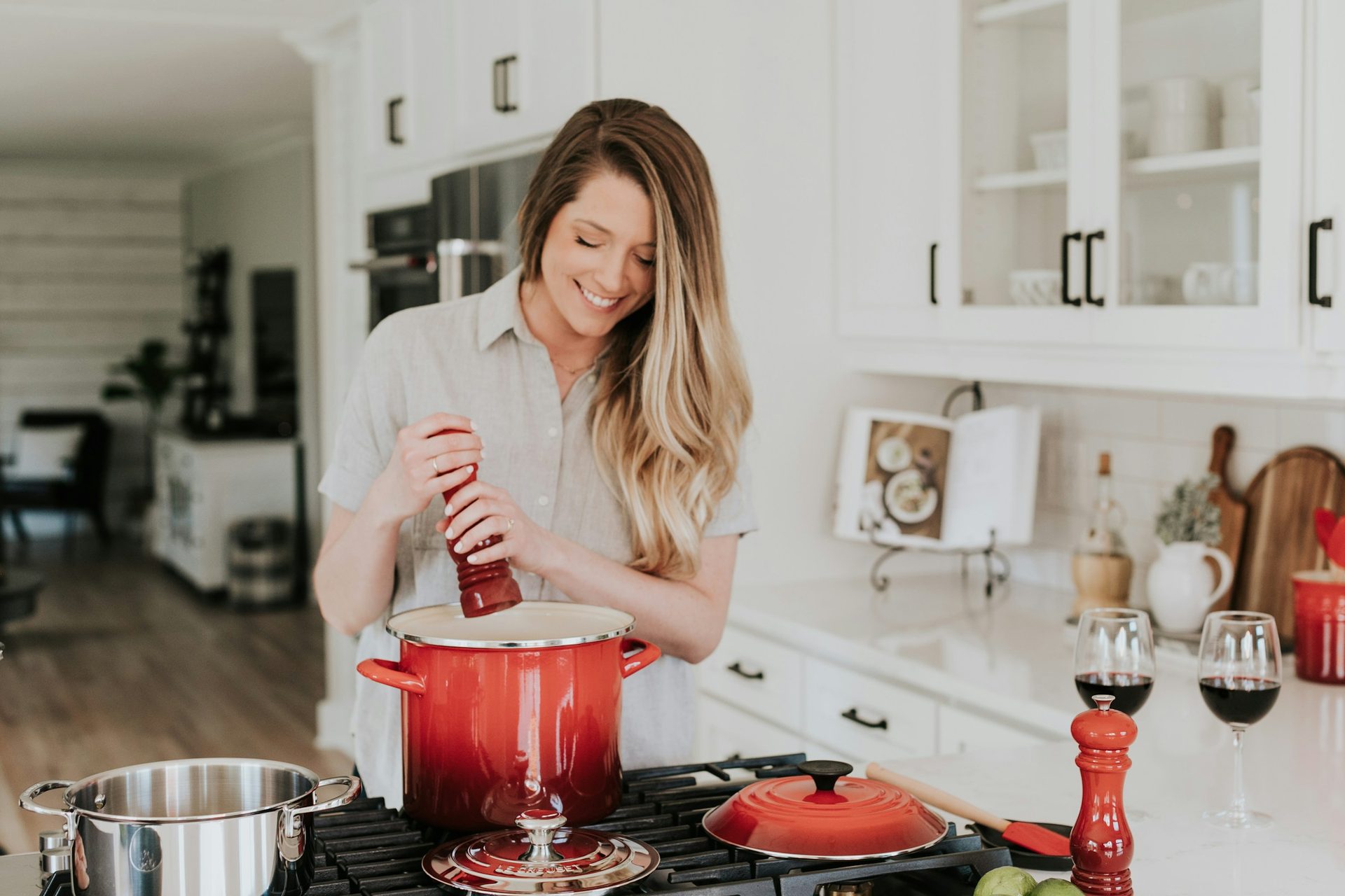 A woman smiling as she grinds pepper into a red pot on the stove